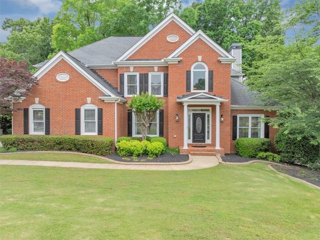 colonial house featuring brick siding, a front yard, and a chimney