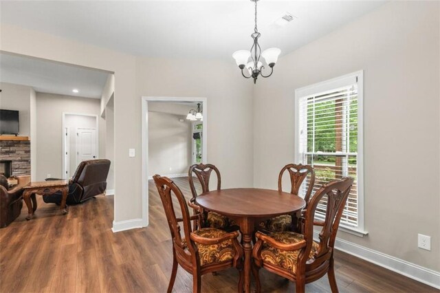 dining area with dark wood-style flooring, baseboards, a notable chandelier, and a fireplace