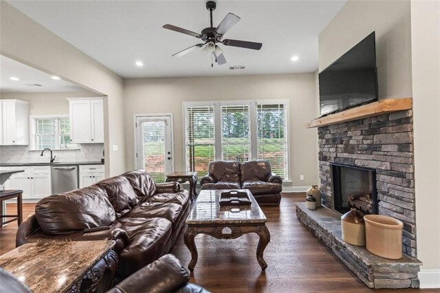 living area featuring recessed lighting, ceiling fan, a stone fireplace, and dark wood-type flooring