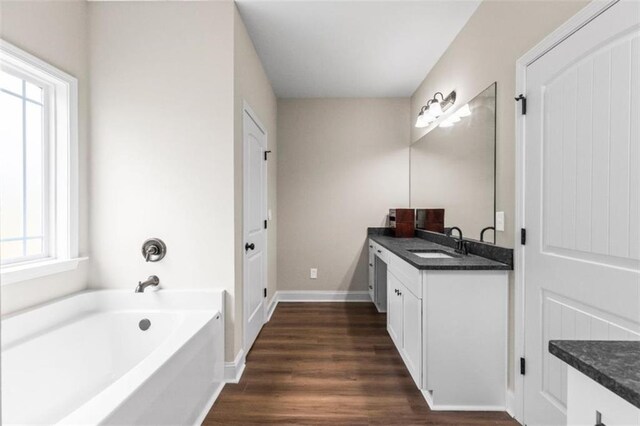 bathroom with vanity, baseboards, a bath, and wood finished floors