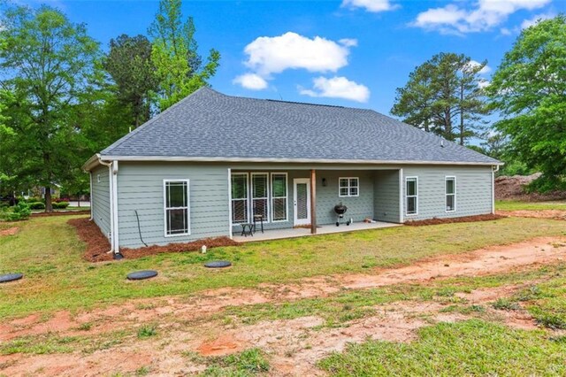 rear view of property featuring roof with shingles, a yard, and a patio area