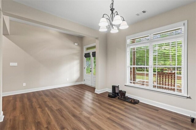 unfurnished dining area featuring visible vents, plenty of natural light, an inviting chandelier, and wood finished floors