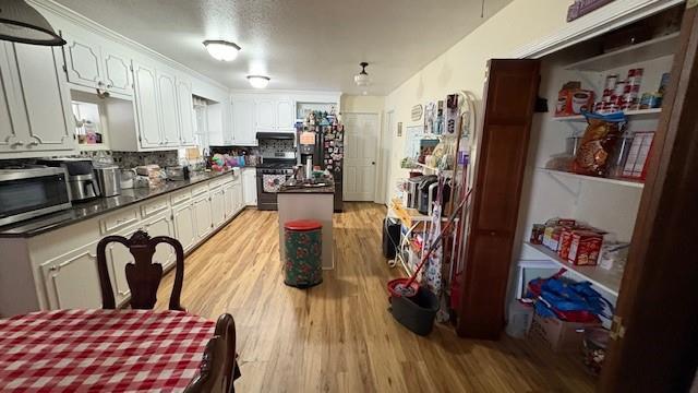 kitchen with dark countertops, backsplash, appliances with stainless steel finishes, light wood-style floors, and white cabinetry