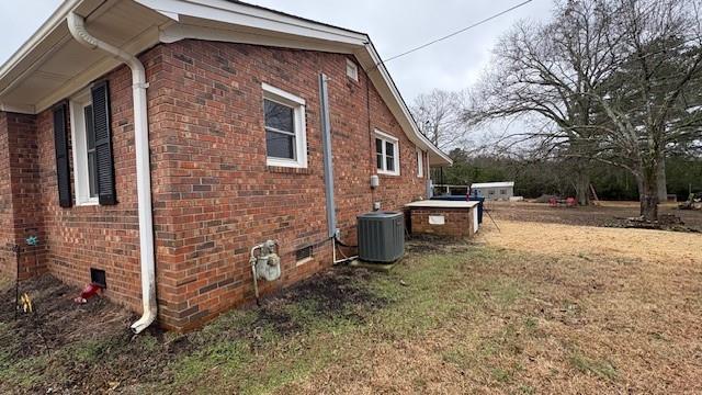 view of side of home featuring crawl space, brick siding, a lawn, and central AC unit