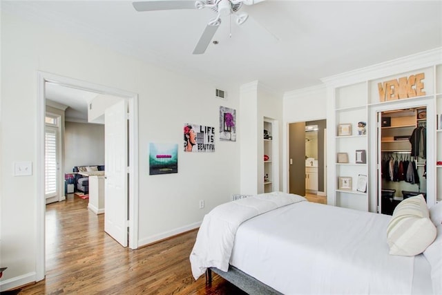 bedroom with wood finished floors, visible vents, baseboards, a spacious closet, and ornamental molding