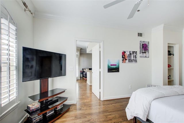 bedroom with baseboards, multiple windows, ornamental molding, and wood finished floors