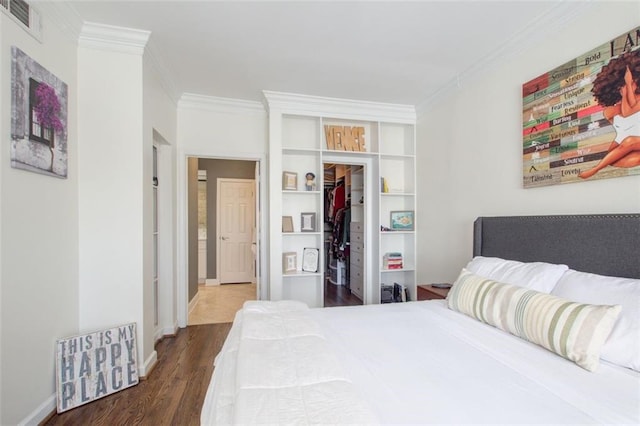 bedroom with visible vents, dark wood finished floors, ornamental molding, a walk in closet, and a closet