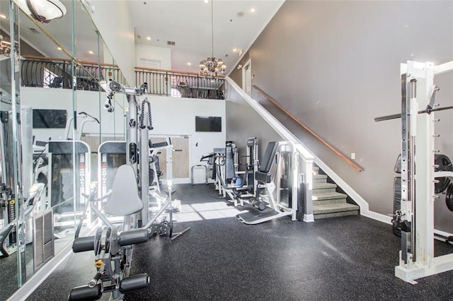 exercise room with a high ceiling, baseboards, visible vents, and a chandelier