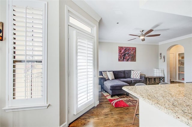 living area with arched walkways, ornamental molding, dark wood-style floors, and a ceiling fan