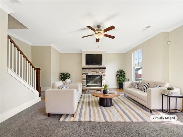 living room with carpet floors, a stone fireplace, ceiling fan, and ornamental molding