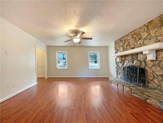 unfurnished living room with ceiling fan, a stone fireplace, hardwood / wood-style floors, and a textured ceiling