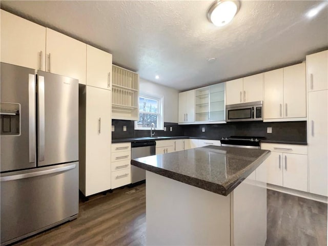 kitchen featuring dark wood-type flooring, white cabinetry, a center island, appliances with stainless steel finishes, and decorative backsplash