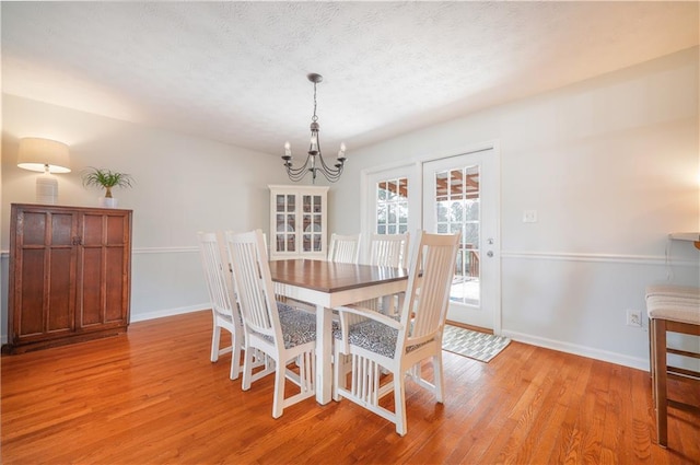 dining room featuring an inviting chandelier, light wood-style flooring, baseboards, and a textured ceiling