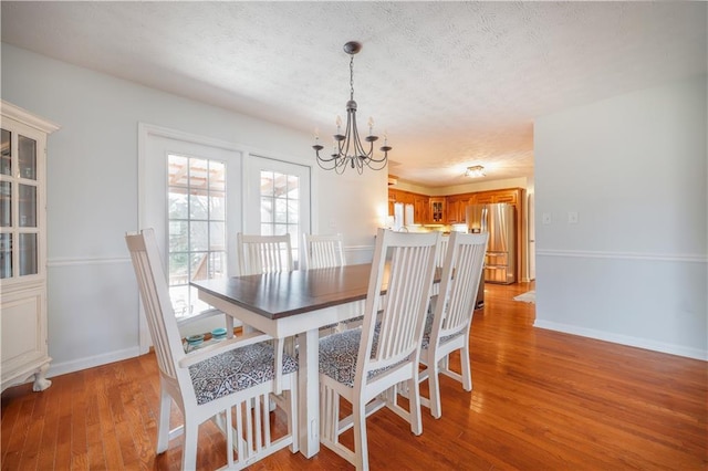 dining space with baseboards, a textured ceiling, light wood finished floors, and an inviting chandelier