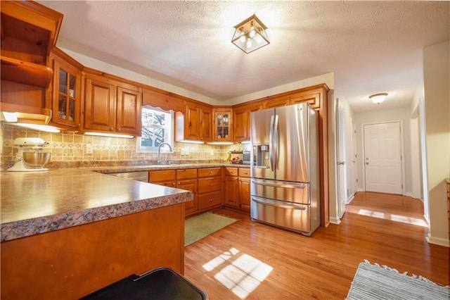 kitchen featuring stainless steel appliances, glass insert cabinets, light wood-style flooring, and brown cabinets