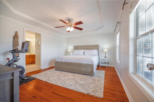 bedroom featuring ceiling fan, ensuite bathroom, wood finished floors, baseboards, and crown molding