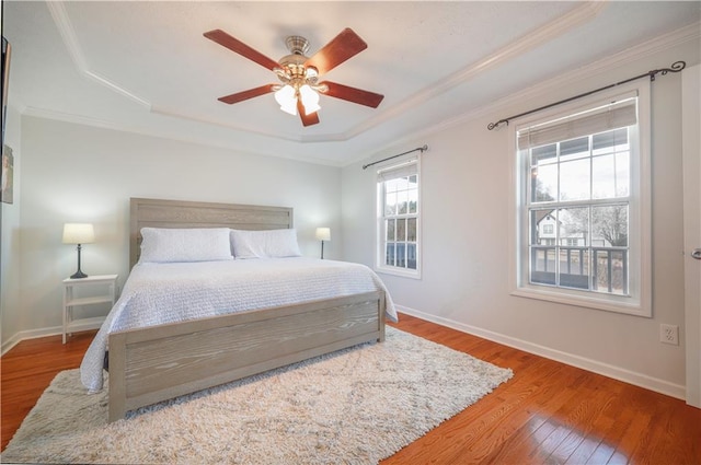 bedroom with ornamental molding, a tray ceiling, baseboards, and hardwood / wood-style flooring