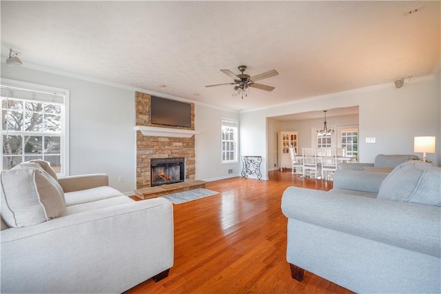 living room featuring a fireplace, ornamental molding, light wood-type flooring, baseboards, and ceiling fan with notable chandelier