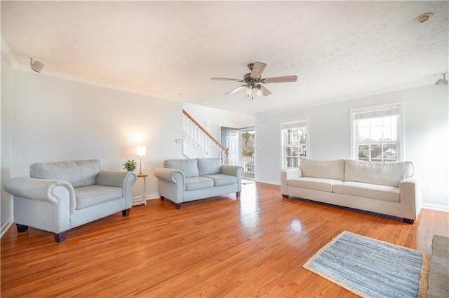 living area featuring light wood-style floors, ceiling fan, a textured ceiling, baseboards, and stairs