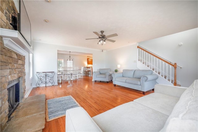 living room featuring a ceiling fan, a stone fireplace, stairway, and wood finished floors