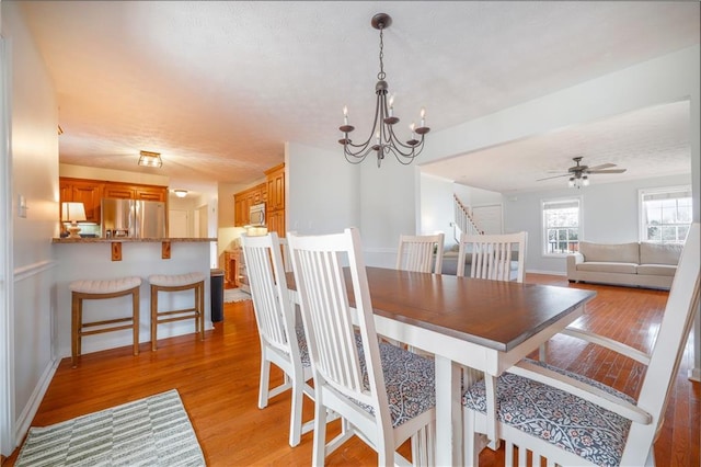 dining area with light wood-style floors, stairs, baseboards, and ceiling fan with notable chandelier