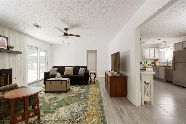 340 Monivea Ln, Roswell, GA 30075 - living room featuring a ceiling fan, a fireplace, a textured ceiling, light wood finished floors, and baseboards
