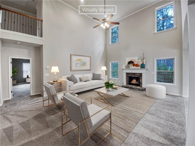 living room featuring a towering ceiling, a fireplace, carpet floors, and ceiling fan