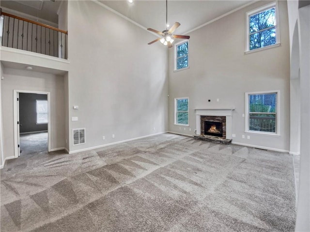 unfurnished living room featuring a high ceiling, crown molding, carpet flooring, a fireplace, and ceiling fan