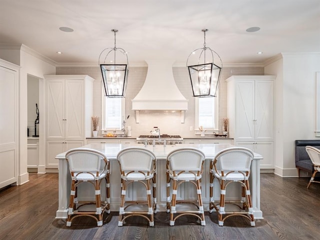 kitchen with light countertops, premium range hood, an island with sink, and pendant lighting