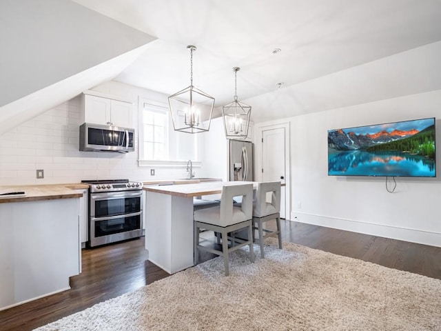 kitchen featuring a breakfast bar area, butcher block counters, white cabinets, appliances with stainless steel finishes, and decorative light fixtures