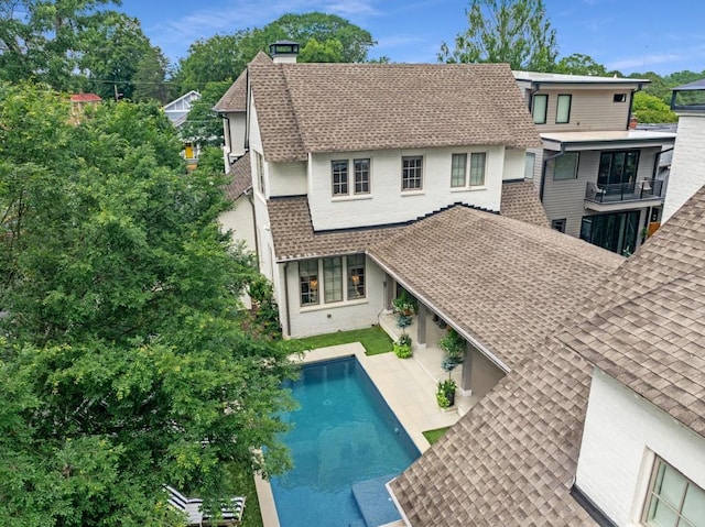 rear view of house featuring a patio area, roof with shingles, a chimney, and an outdoor pool