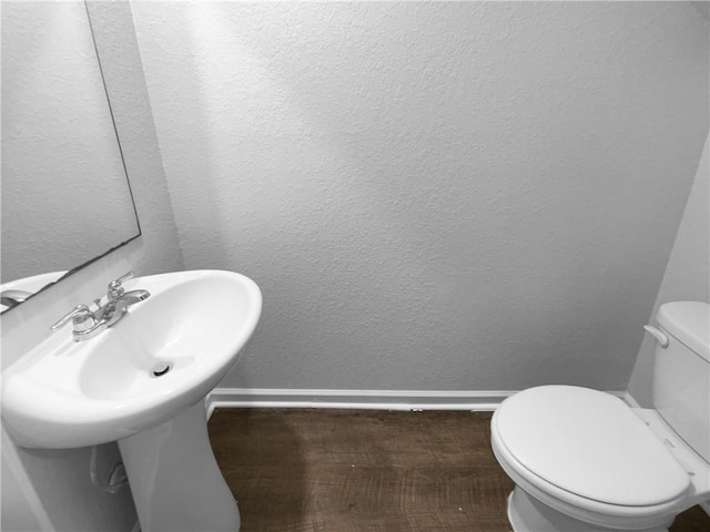 half bathroom with a textured wall, toilet, and baseboards