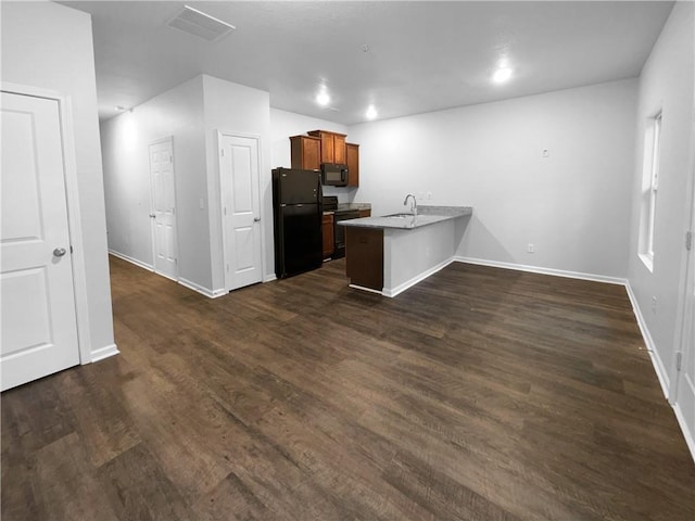 kitchen featuring brown cabinetry, dark wood-type flooring, black appliances, a peninsula, and baseboards