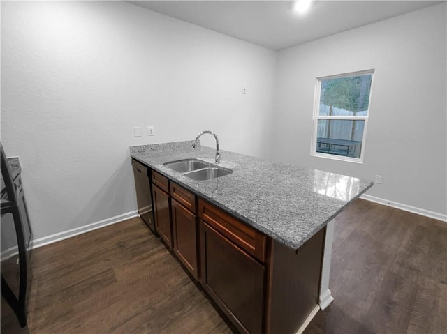 kitchen featuring a peninsula, dark wood-type flooring, a sink, baseboards, and dishwasher
