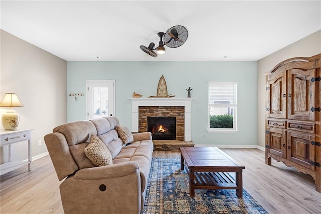 living area with baseboards, a ceiling fan, light wood finished floors, and a fireplace