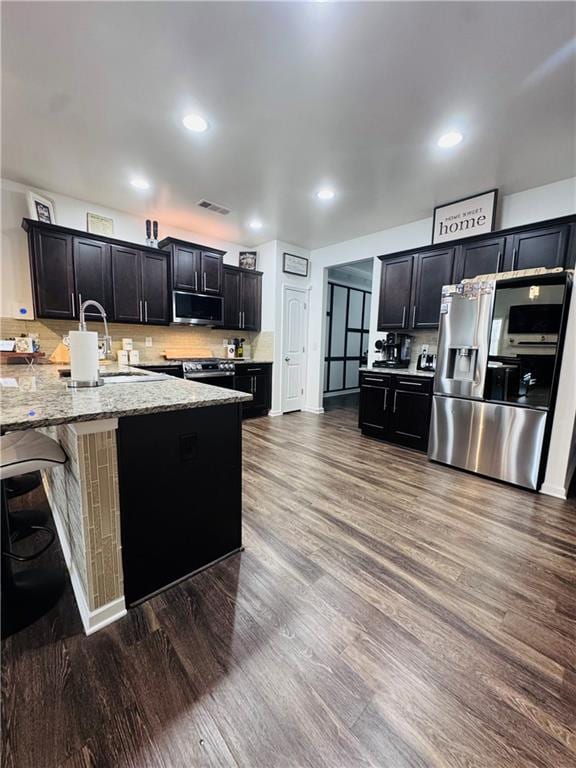 kitchen with sink, wood-type flooring, stainless steel appliances, light stone countertops, and decorative backsplash