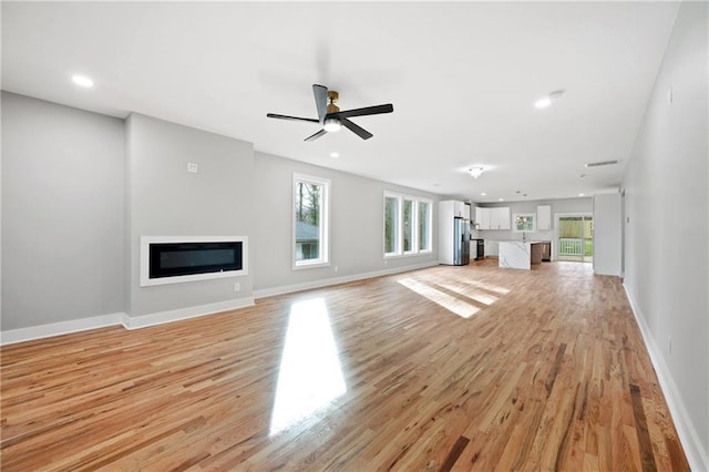 unfurnished living room featuring a glass covered fireplace, light wood-style flooring, baseboards, and recessed lighting