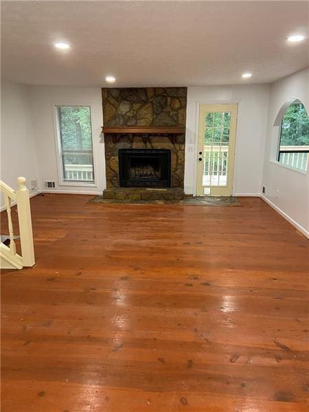 unfurnished living room featuring a healthy amount of sunlight, hardwood / wood-style flooring, a fireplace, and stairway