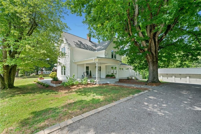 view of front of house featuring covered porch, an outbuilding, a garage, and a front yard