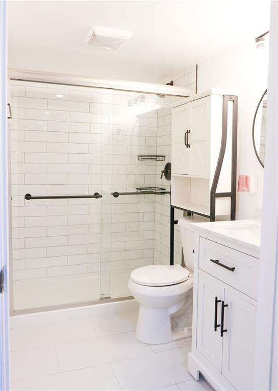 bathroom with tile patterned floors, vanity, toilet, and a shower with door