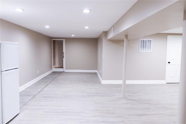 basement with white refrigerator and light hardwood / wood-style flooring