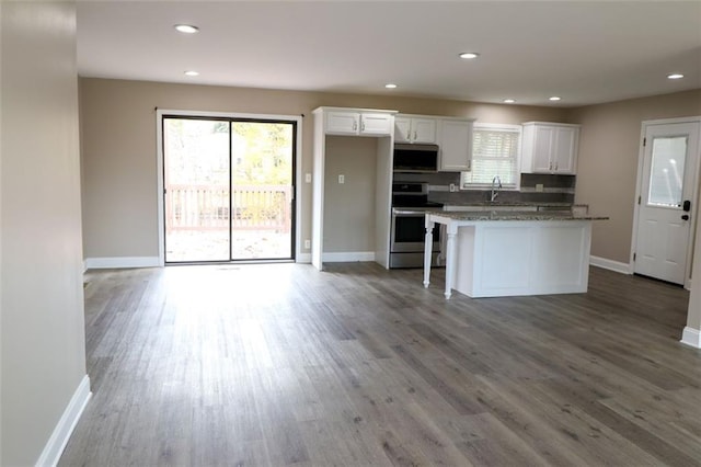 kitchen featuring dark stone counters, a breakfast bar, stainless steel appliances, hardwood / wood-style flooring, and white cabinetry