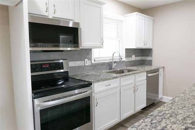 kitchen with backsplash, sink, light stone countertops, white cabinetry, and stainless steel appliances