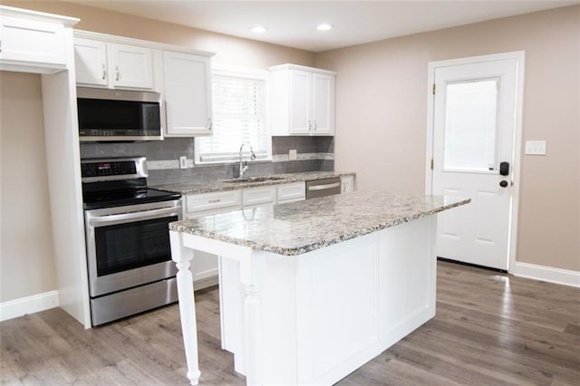 kitchen featuring white cabinetry, stainless steel appliances, decorative backsplash, a kitchen island, and light wood-type flooring