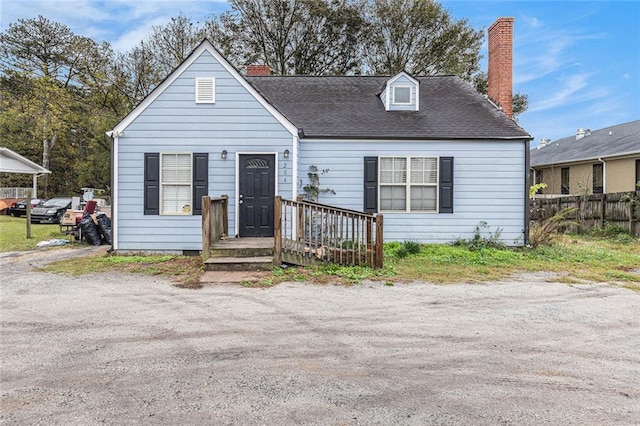 cape cod home featuring driveway, a shingled roof, a chimney, and fence