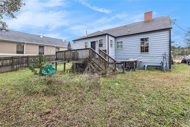 rear view of house featuring roof with shingles, a chimney, a lawn, fence, and a wooden deck