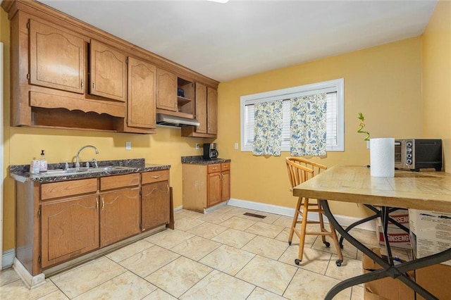 kitchen featuring baseboards, dark countertops, brown cabinets, open shelves, and a sink