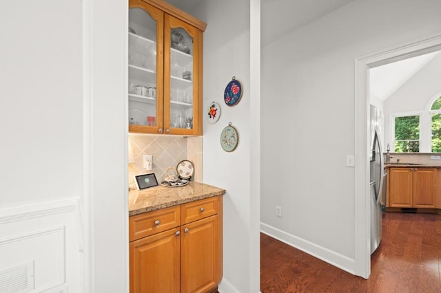 bar with stainless steel refrigerator, light stone countertops, dark wood-type flooring, lofted ceiling, and decorative backsplash