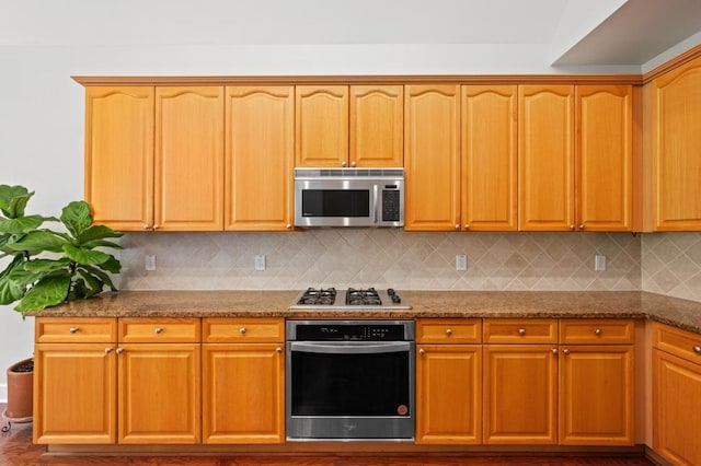 kitchen featuring backsplash, dark stone counters, and appliances with stainless steel finishes