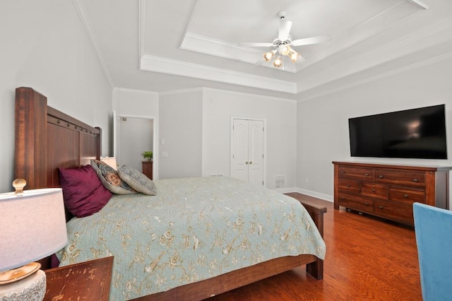 bedroom with a tray ceiling, ceiling fan, crown molding, hardwood / wood-style flooring, and a closet